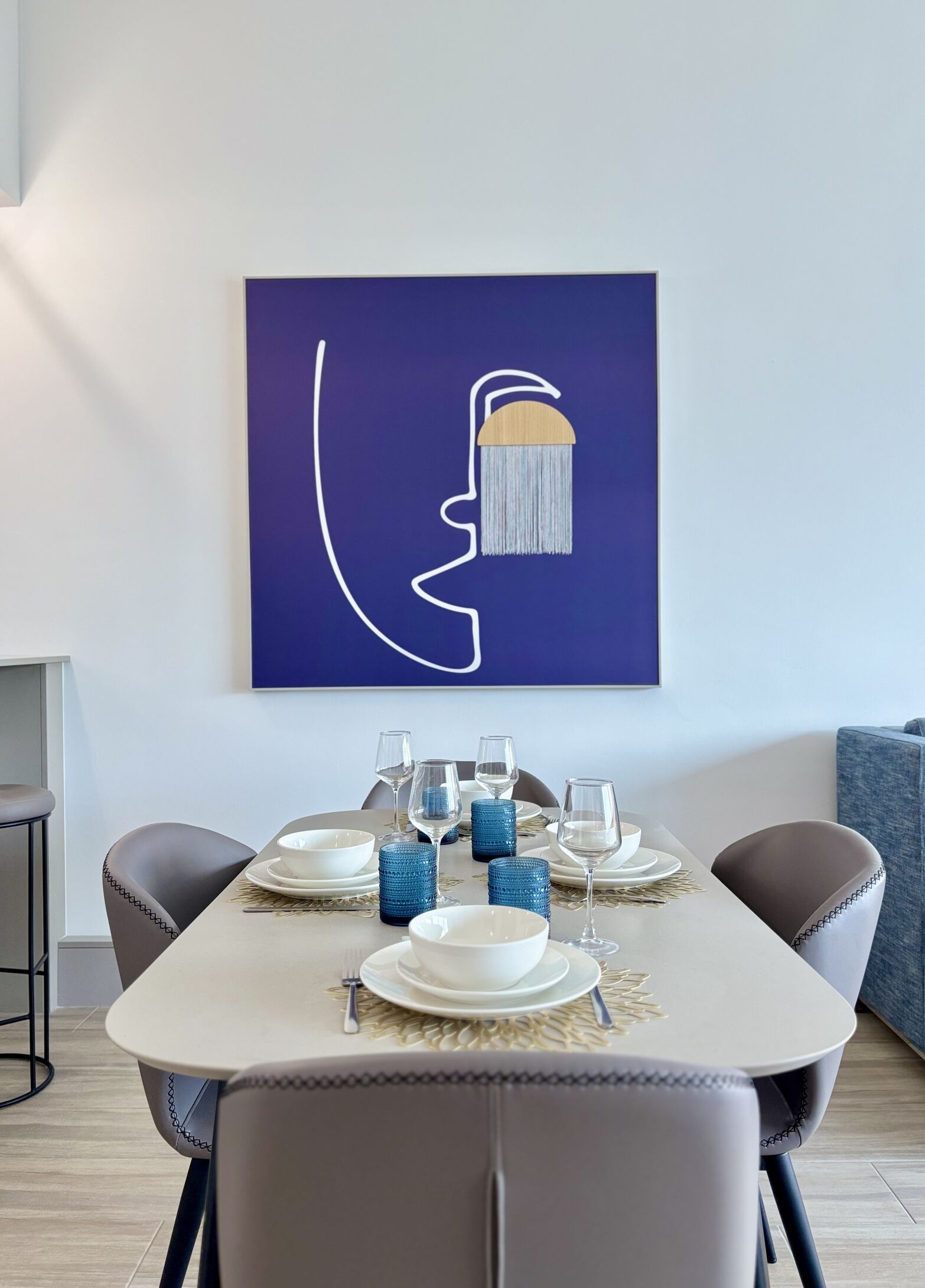 A dining area with a table set for multiple people, chairs, and artwork on the wall.