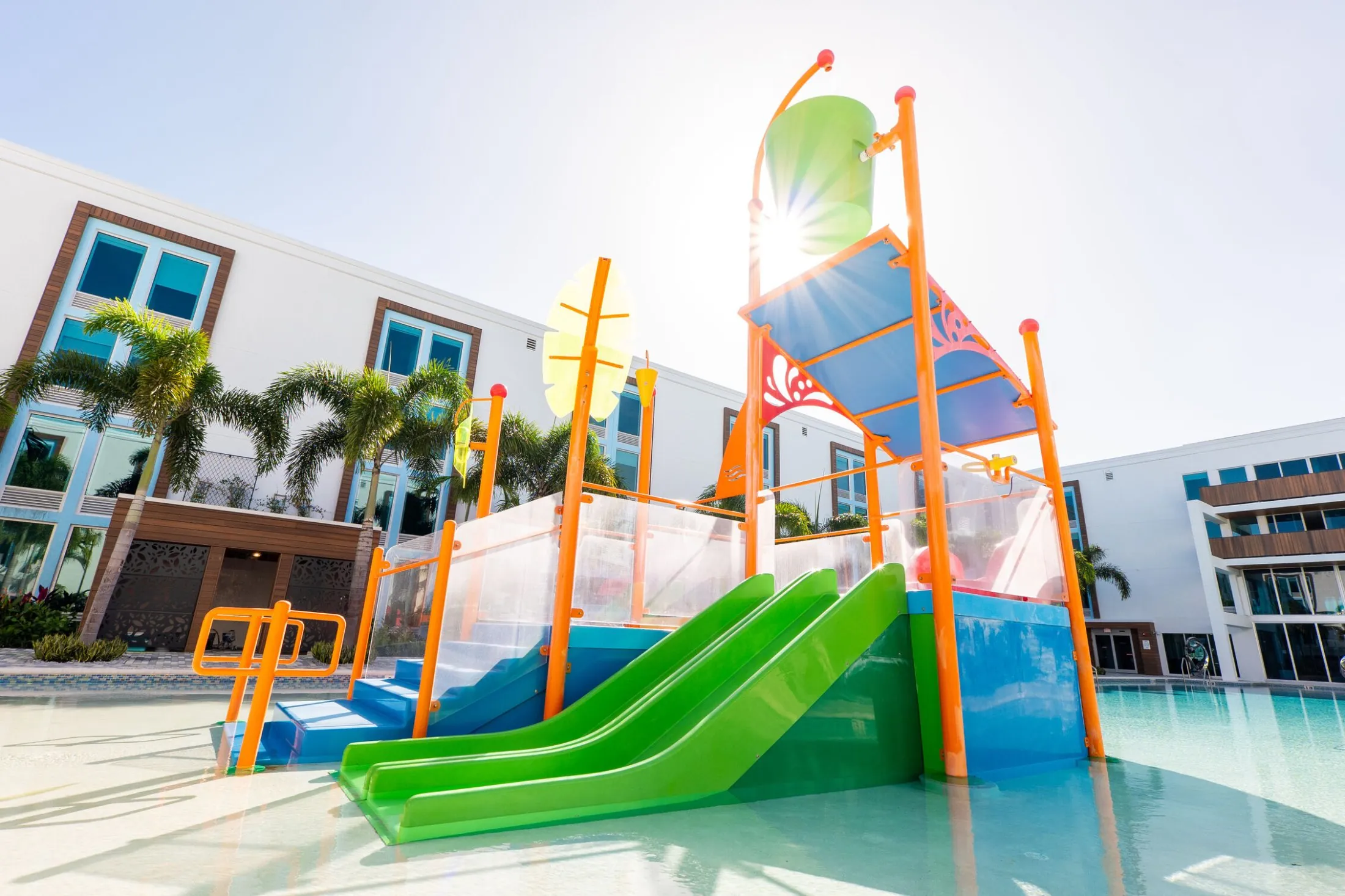 A colorful water slide and play structure in a pool area with a building in the background.