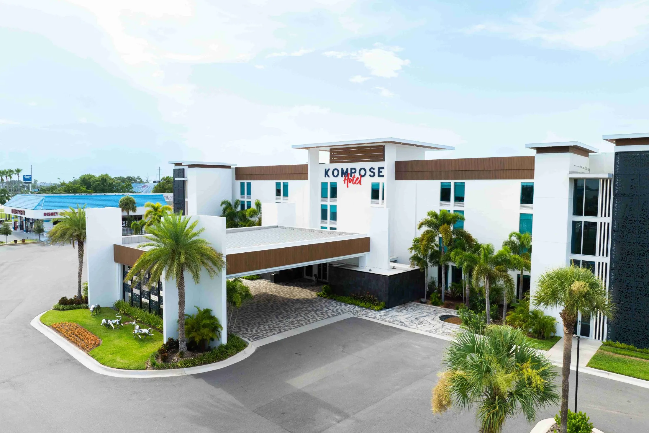 A wide exterior view of a white hotel building with brown accents and palm trees.