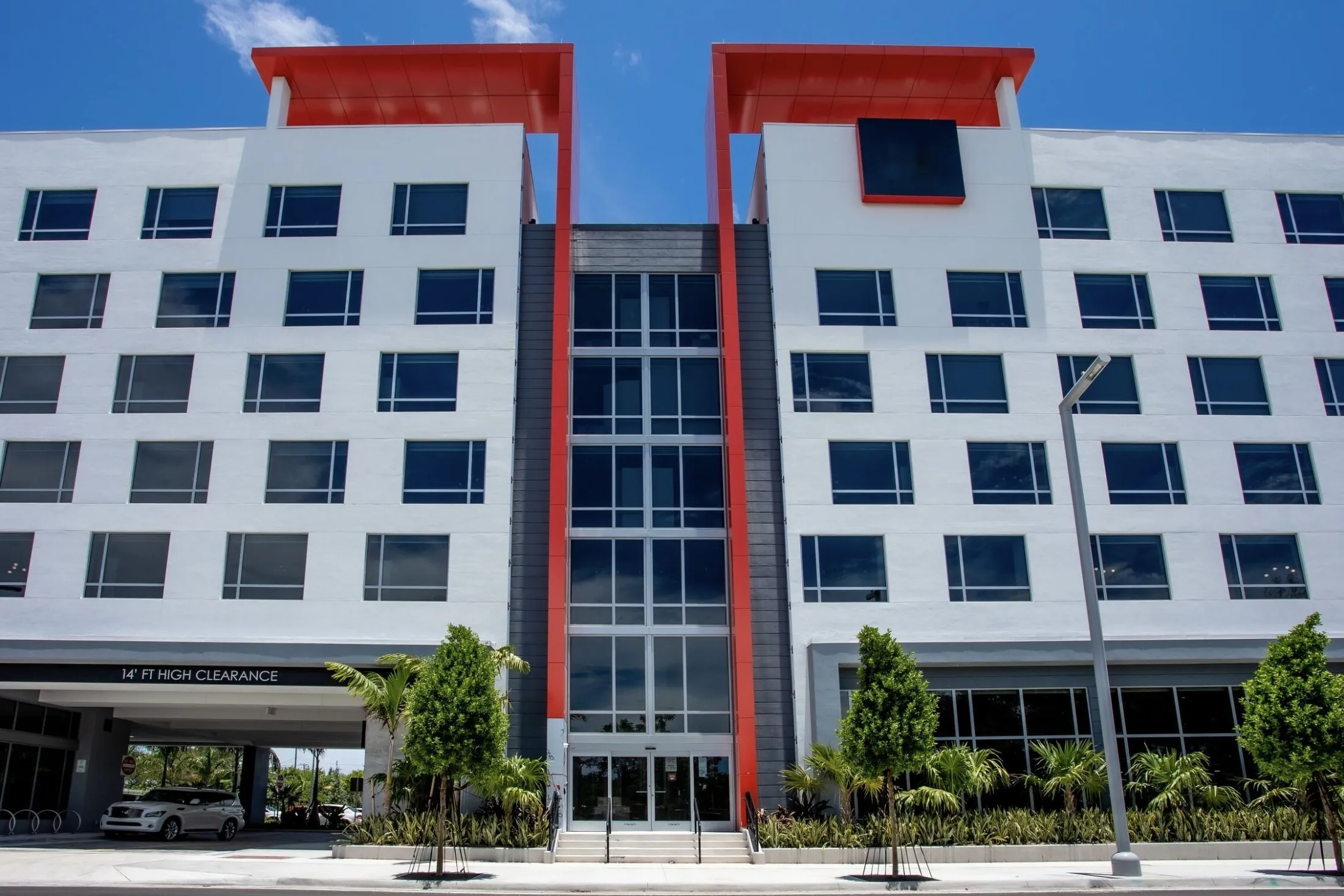 A large white building with red accents and a parking lot in front.