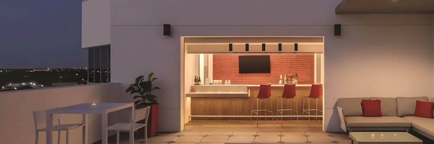 A modern outdoor lounge area with a bar, sofa, and coffee table at dusk.